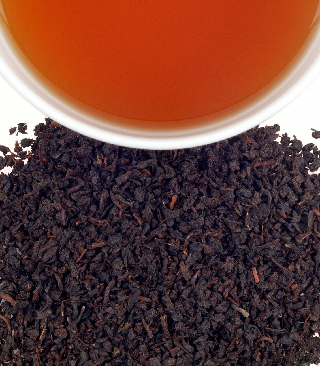 Rich black tea leaves from Uva Highlands with a brewed cup of amber tea above, showcasing its vibrant color.