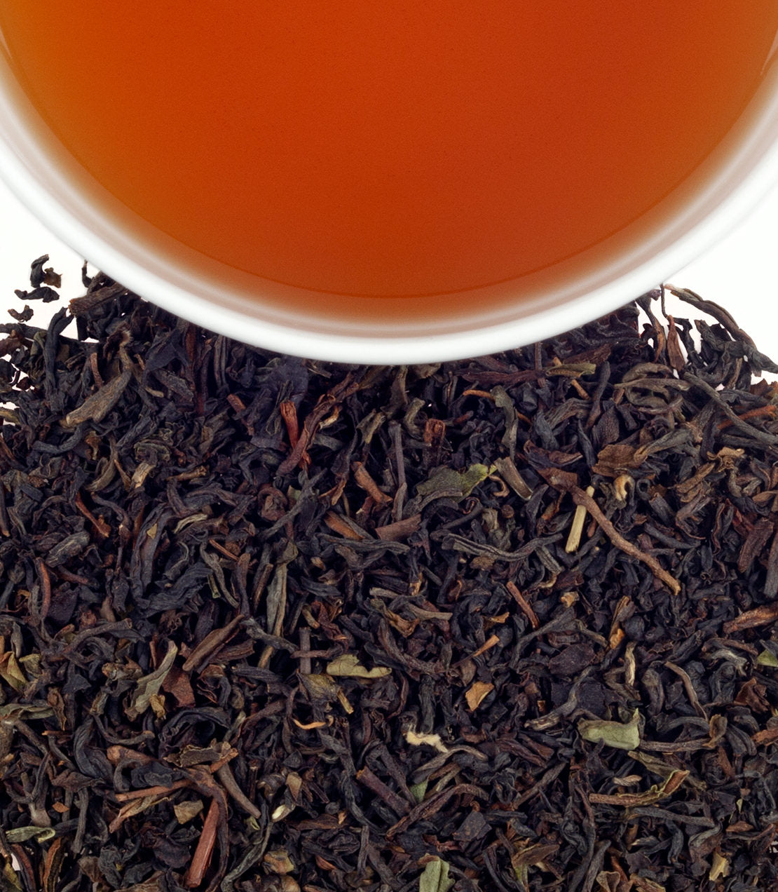 A close-up of loose black tea leaves with a cup of brewed Viennese Earl Grey tea above, showcasing its rich color.