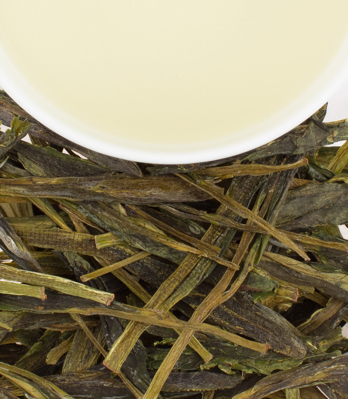 Fresh Taiping Houkui green tea leaves with a cup of pale yellow tea above, showcasing its unique flat shape.