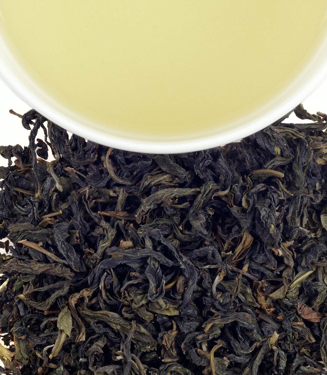Wenshan Baozhong tea leaves with a cup of pale yellow brewed tea above, showcasing its unique color and texture.