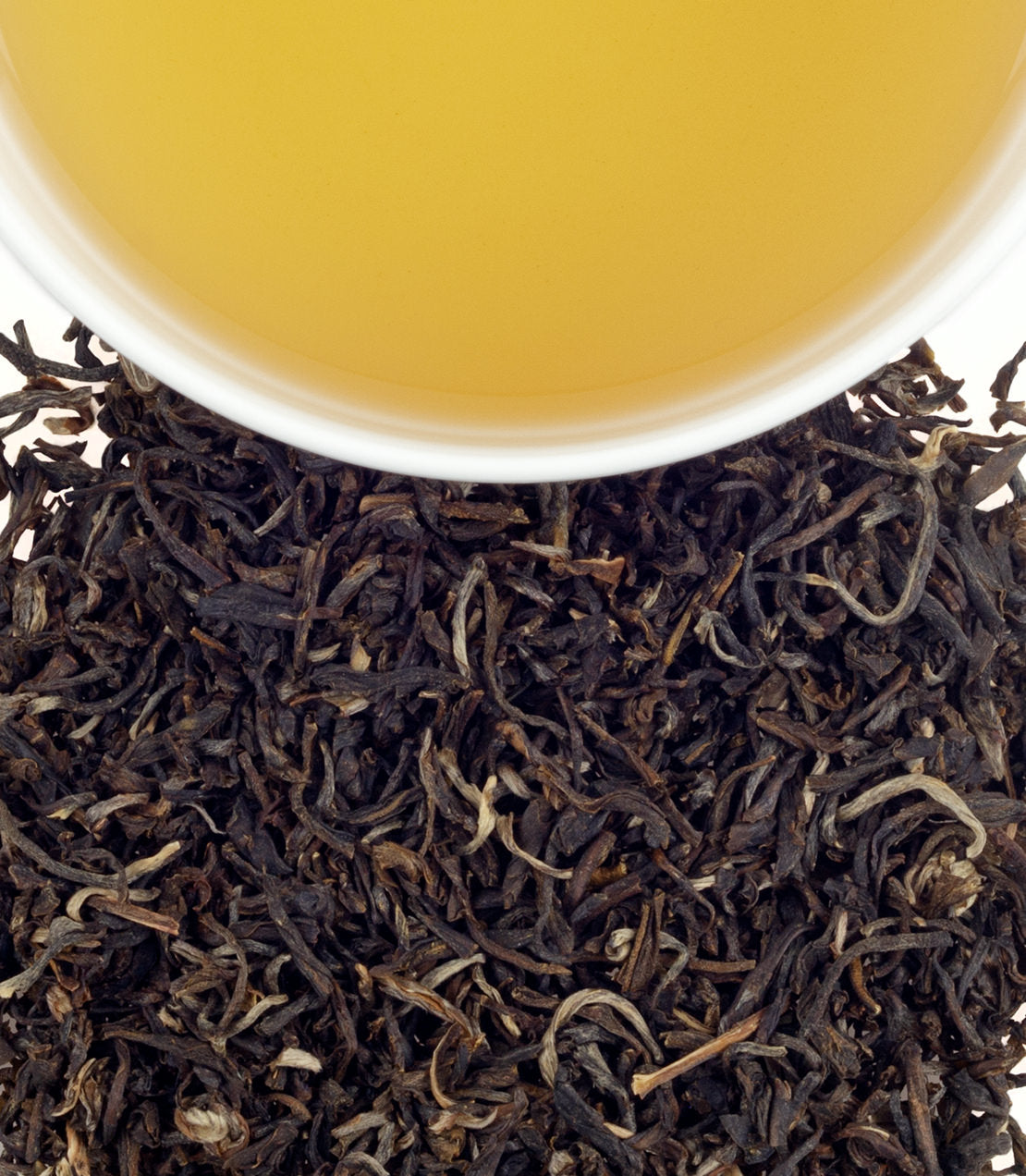 A cup of Yin Hao Jasmine tea above a bed of loose black tea leaves, showcasing its golden hue.