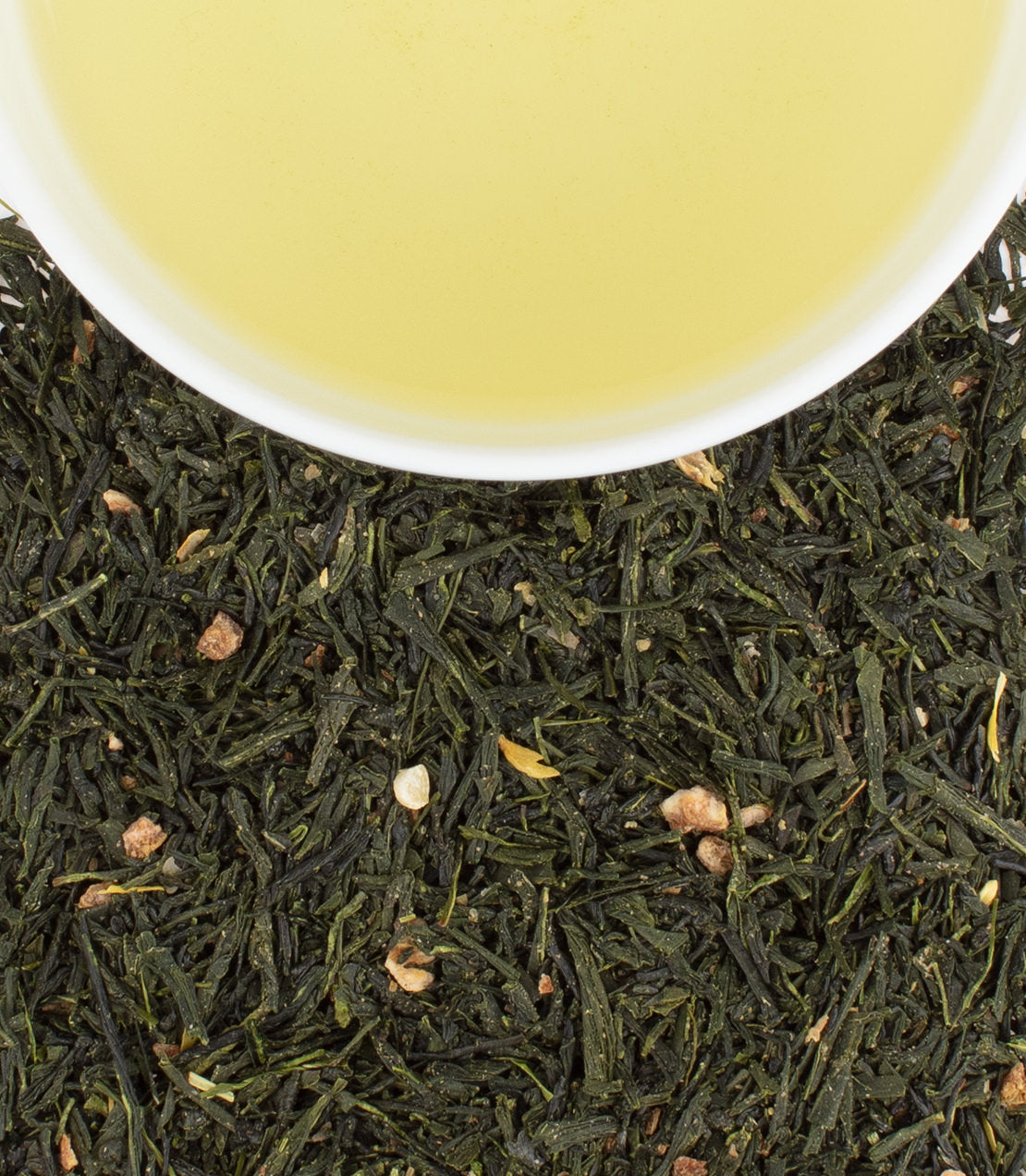 A cup of Yuzu Sencha green tea above loose tea leaves, showcasing vibrant green color and citrusy ingredients.