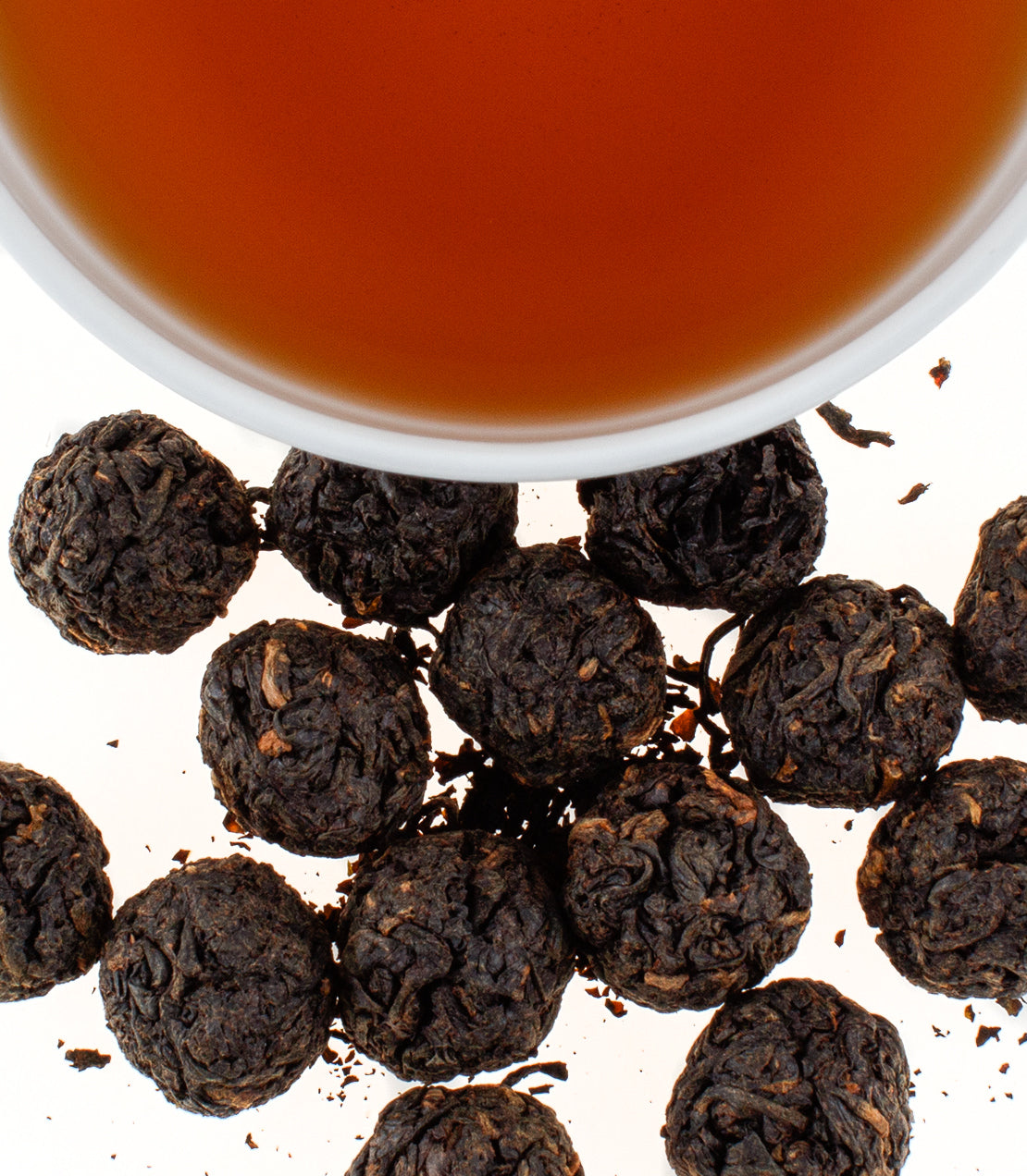 Black Amba Gems tea balls scattered around a cup of brewed tea, showcasing their unique texture and color.