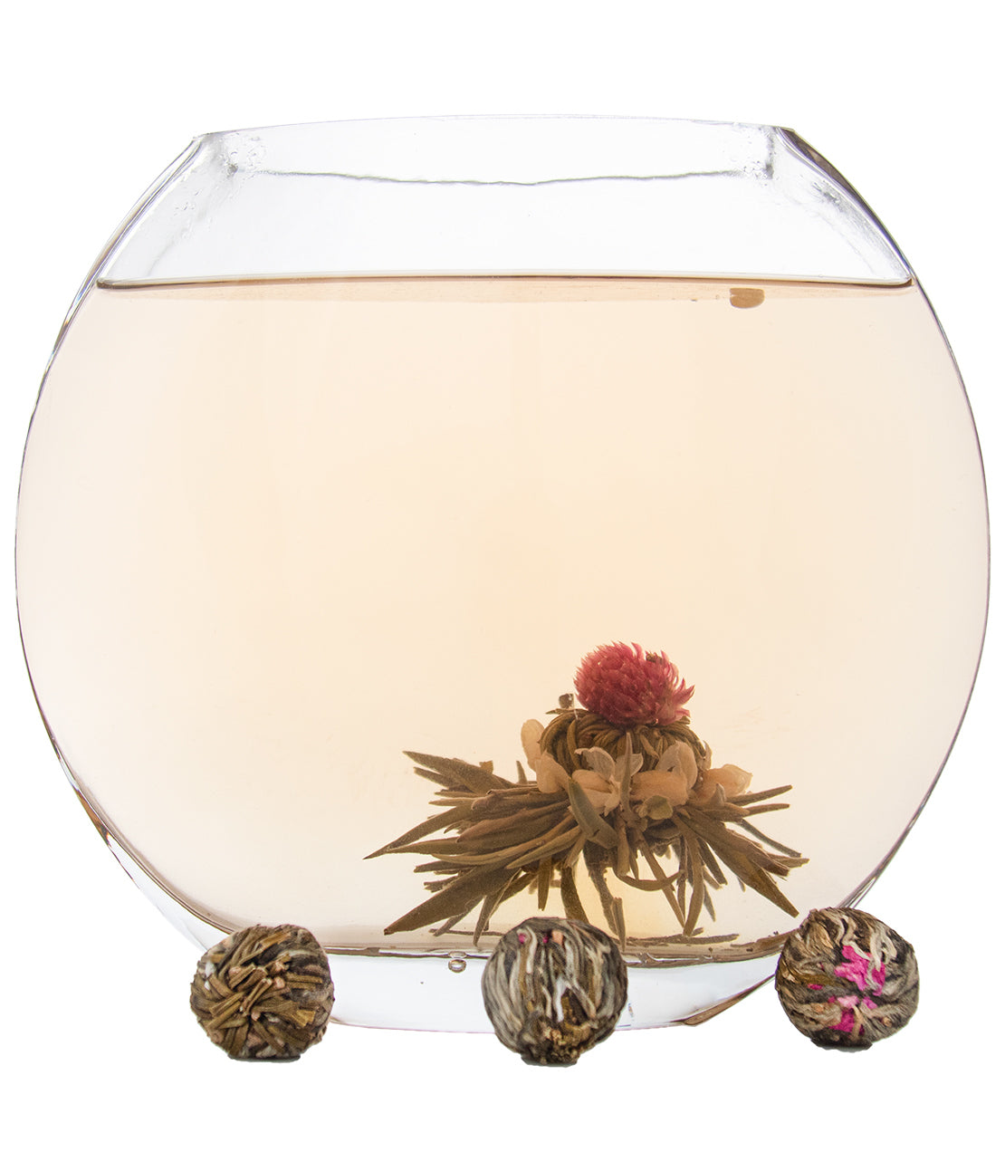 A glass teapot filled with light-colored tea, featuring blooming tea balls and a flower centerpiece.