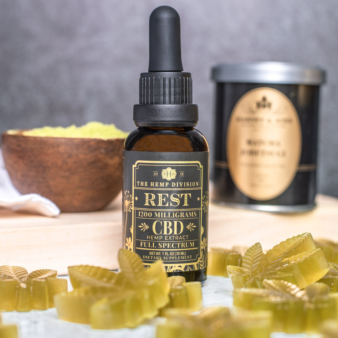 Extra strength hemp extract tincture (3000 MG) in a dropper bottle, surrounded by gummy supplements and a jar.