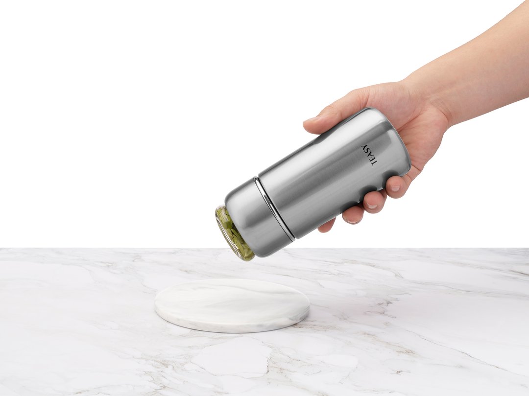 Hand holding a Teasy Insulated Flask over a marble surface, showcasing its sleek design and multiple color options.