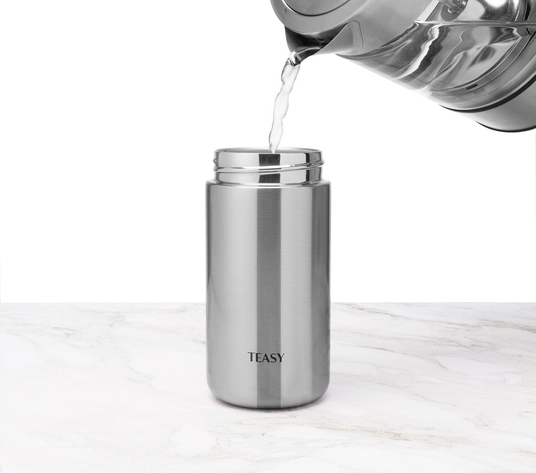 Teasy insulated flask in stainless steel with water being poured into it, set on a marble surface.