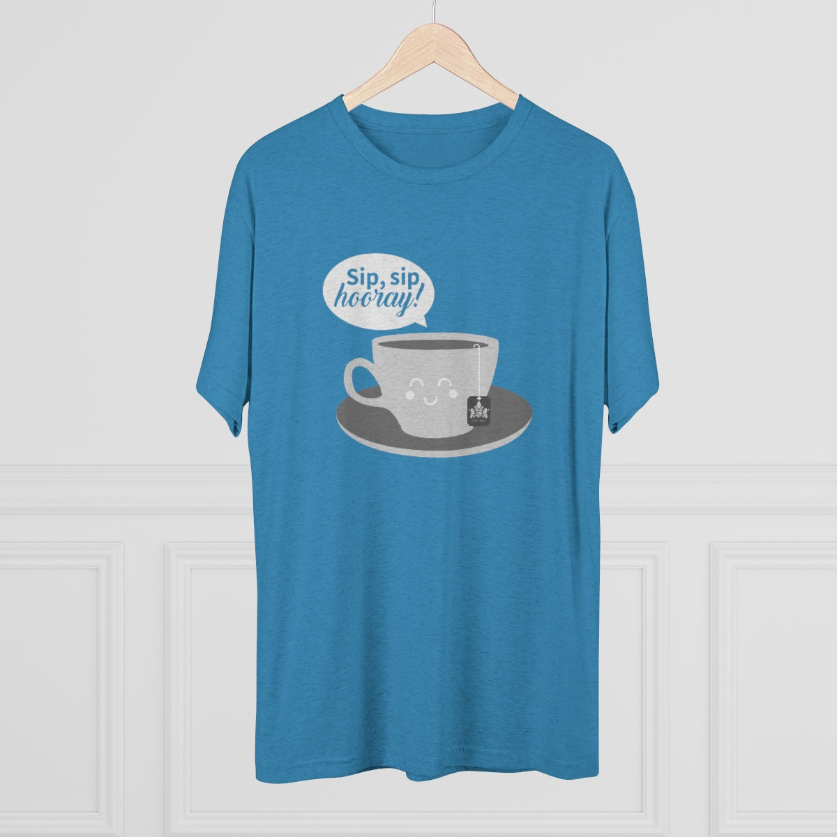 Blue graphic tee featuring a smiling coffee cup and the text "Sip, sip, hooray!" on a wooden hanger.