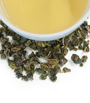 Dong Ding Light oolong tea leaves scattered beside a cup of brewed tea, showcasing its light amber color.