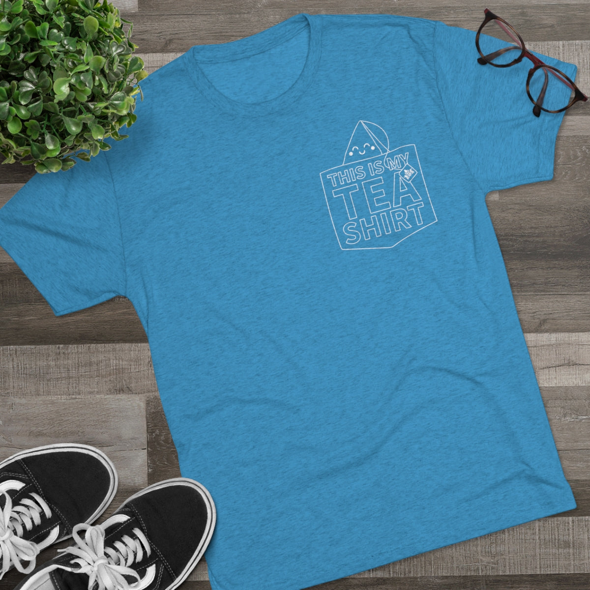 Blue graphic tee featuring the text "This Is My Tea Shirt" with a tea bag illustration, styled on a wooden surface.