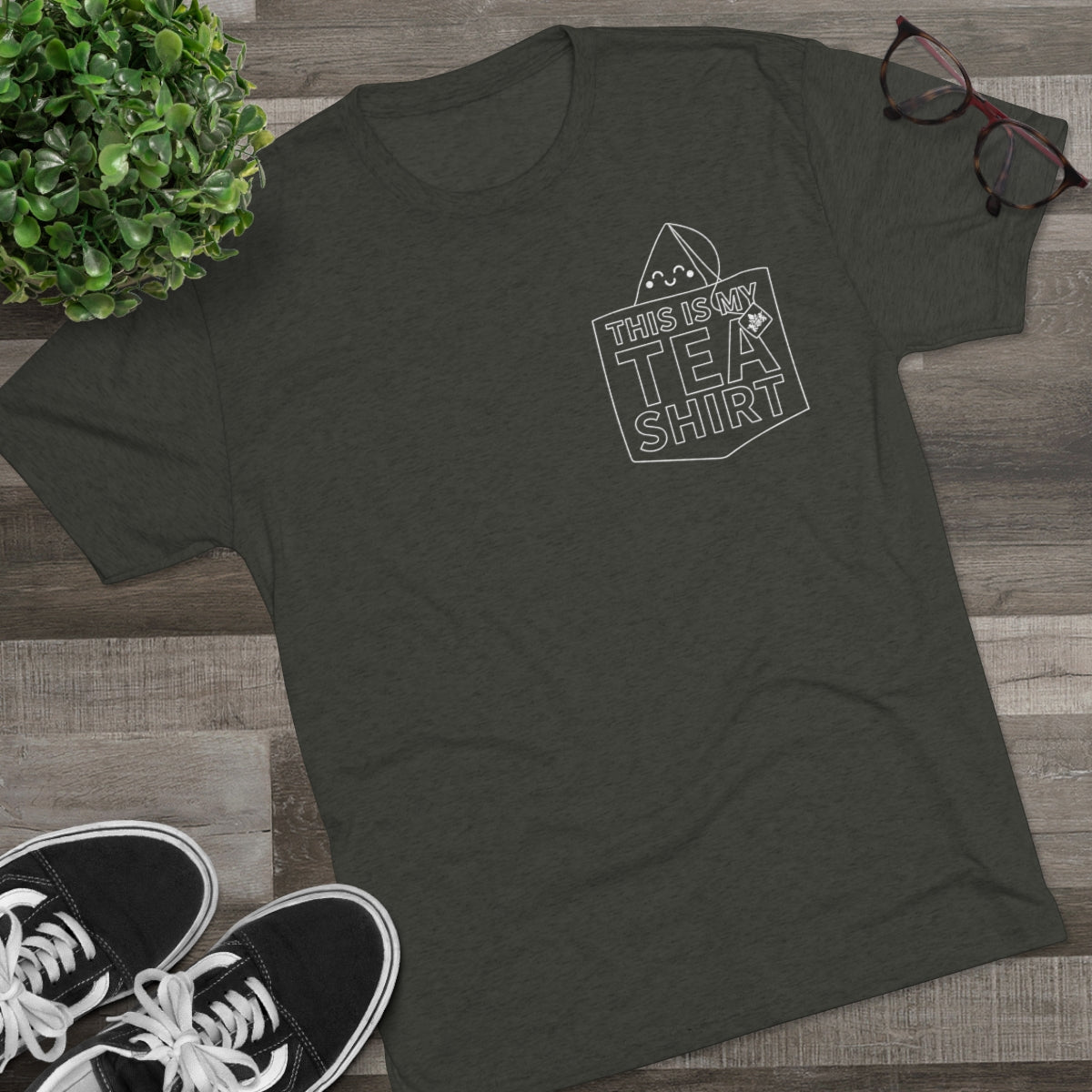Olive green graphic tee with "This Is My Tea Shirt" design, paired with black sneakers and glasses on a wooden surface.