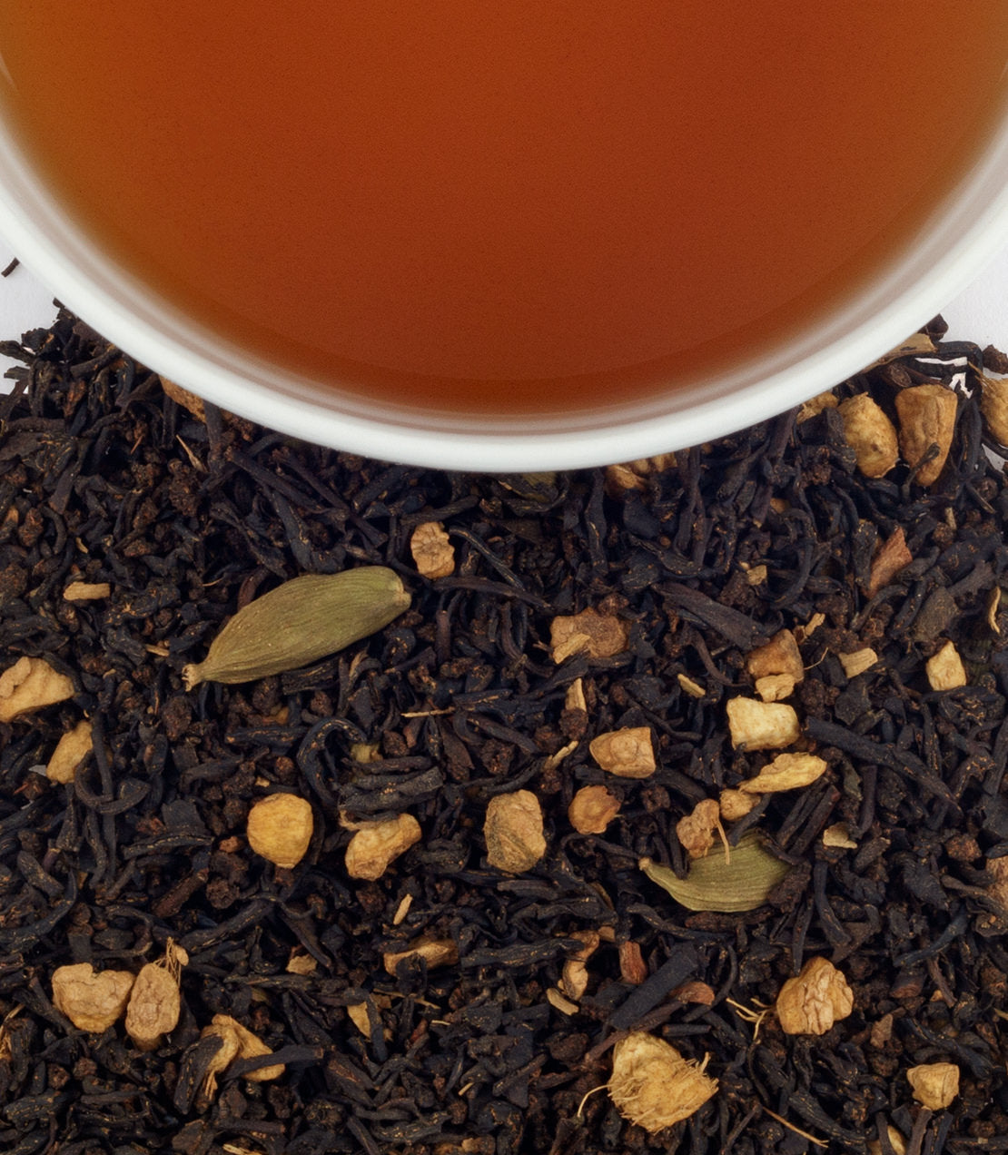 A cup of Chocolate Chai Supreme tea above a bed of loose black tea leaves and spices, showcasing rich flavors.