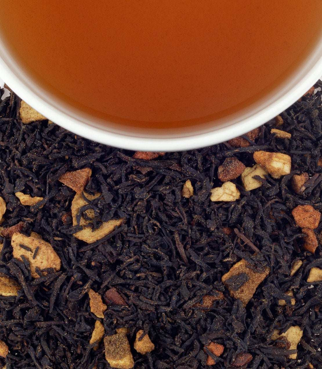 A cup of hot apple spice tea above a bed of loose black tea leaves and apple pieces.