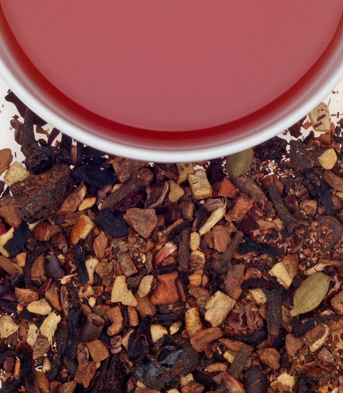 Warm mulled plum cider in a white cup, surrounded by aromatic spices and dried fruit pieces. Perfect for cozy gatherings.
