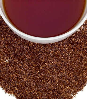 A cup of brewed herbal tea surrounded by loose herbal tea leaves, showcasing rich colors and textures.