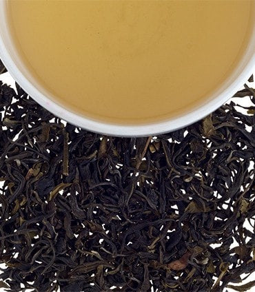 A cup of Colombian green tea surrounded by loose tea leaves, showcasing its light amber color.