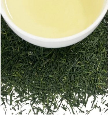 A cup of light green tea surrounded by vibrant, finely cut Gyokuro tea leaves.