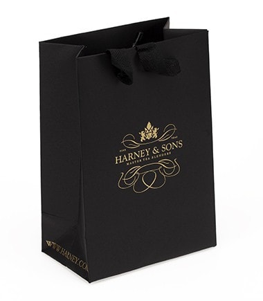Small black shopping bag from Harney & Sons, featuring a gold logo and ribbon handles. Perfect for gifts or purchases.