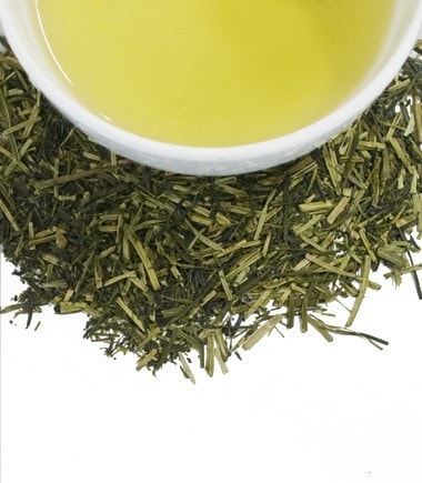 A cup of kukicha tea surrounded by dried green tea twigs and leaves, showcasing its vibrant yellow-green color.