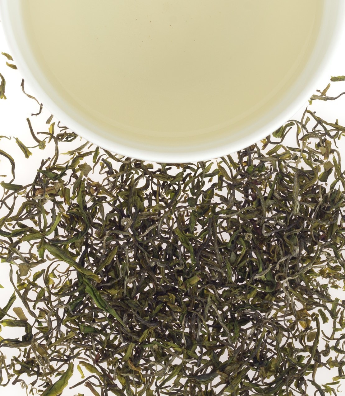 Fresh Tong Lu Green tea leaves scattered beside a cup of light green tea, showcasing its vibrant color and texture.