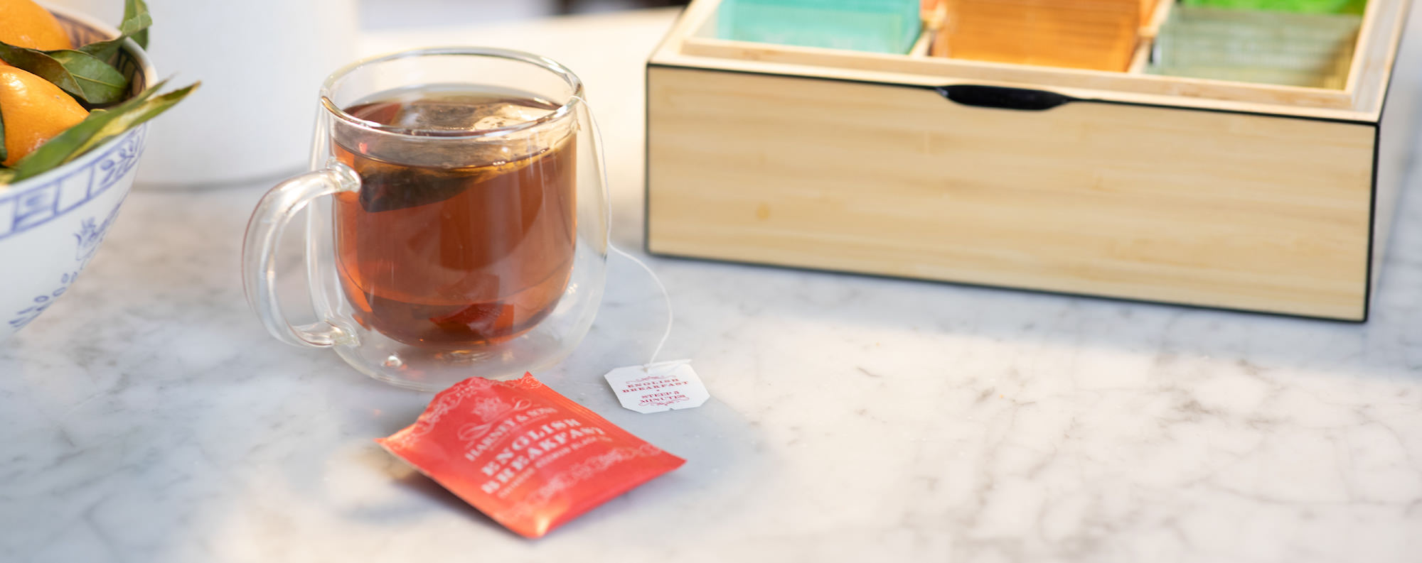 Tea cup with a tea bag on a marble surface next to a wooden box.