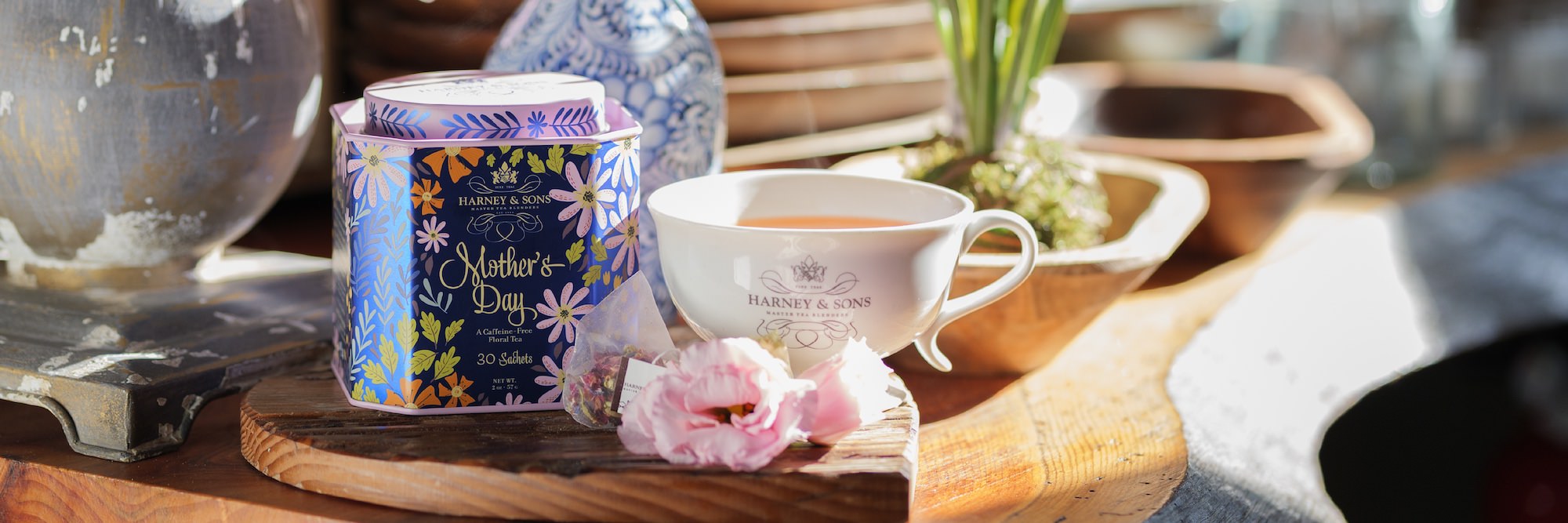 Tea packaging with 'Mother's Day' design next to a cup of tea on a wooden surface.