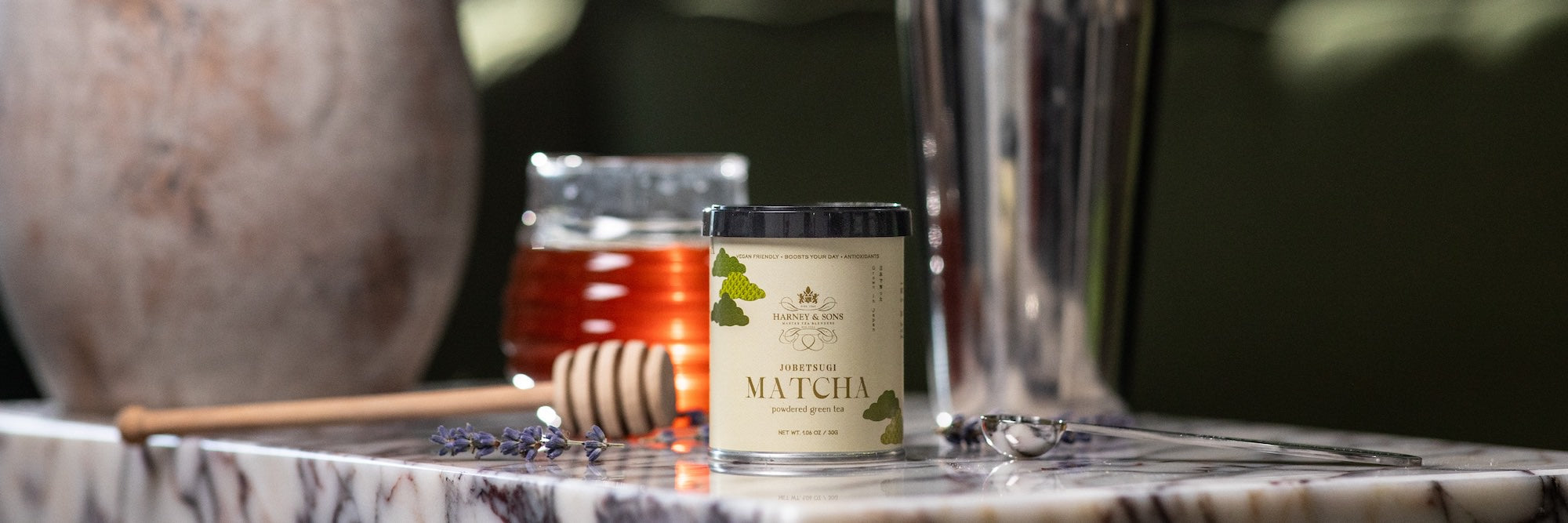 Matcha powder container with a honey dipper and jar of honey on a marble surface.