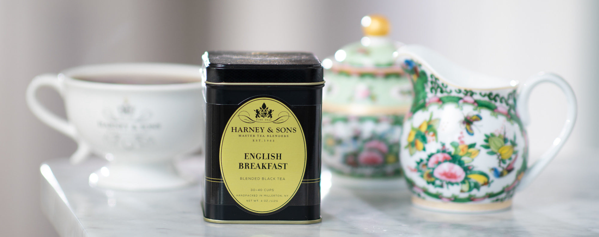 Harney & Sons English Breakfast tea tin on a table with floral teapots in the background.