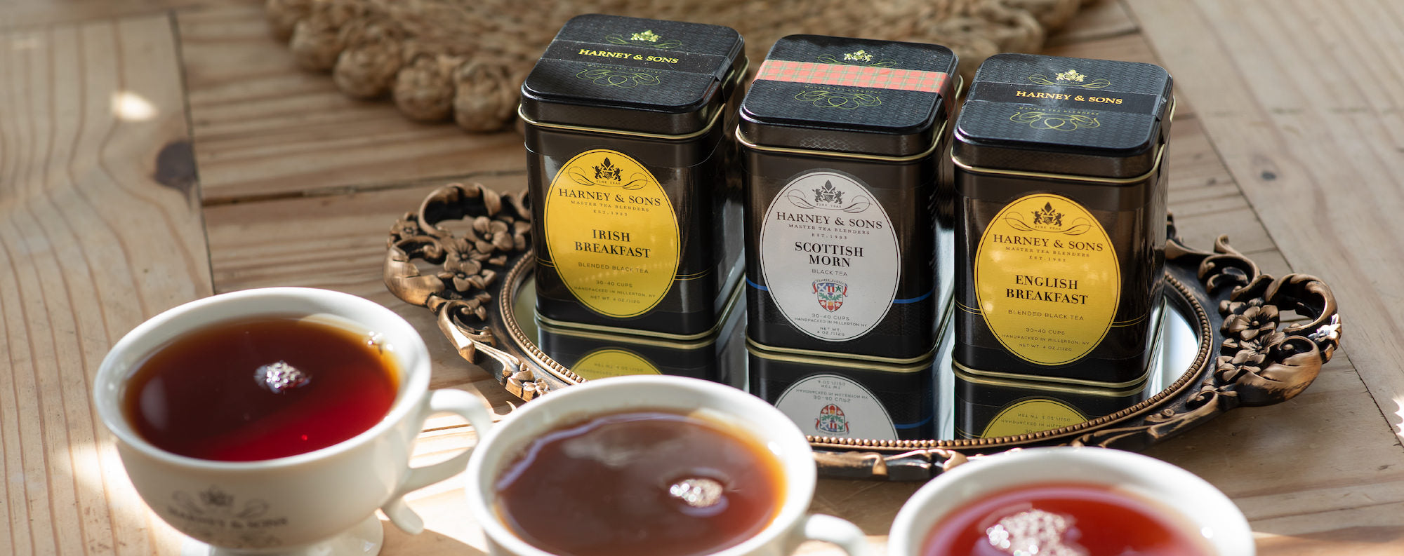 Three tea cups filled with tea and three tea tins on a wooden surface.