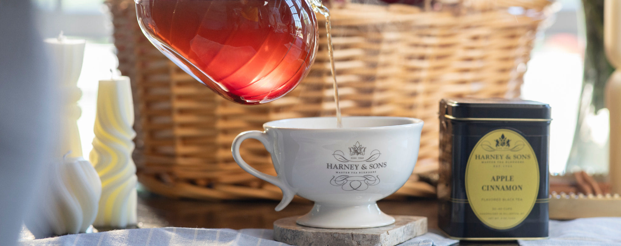 Tea being poured into a Harney & Sons cup with a tin of apple cinnamon tea on a table.