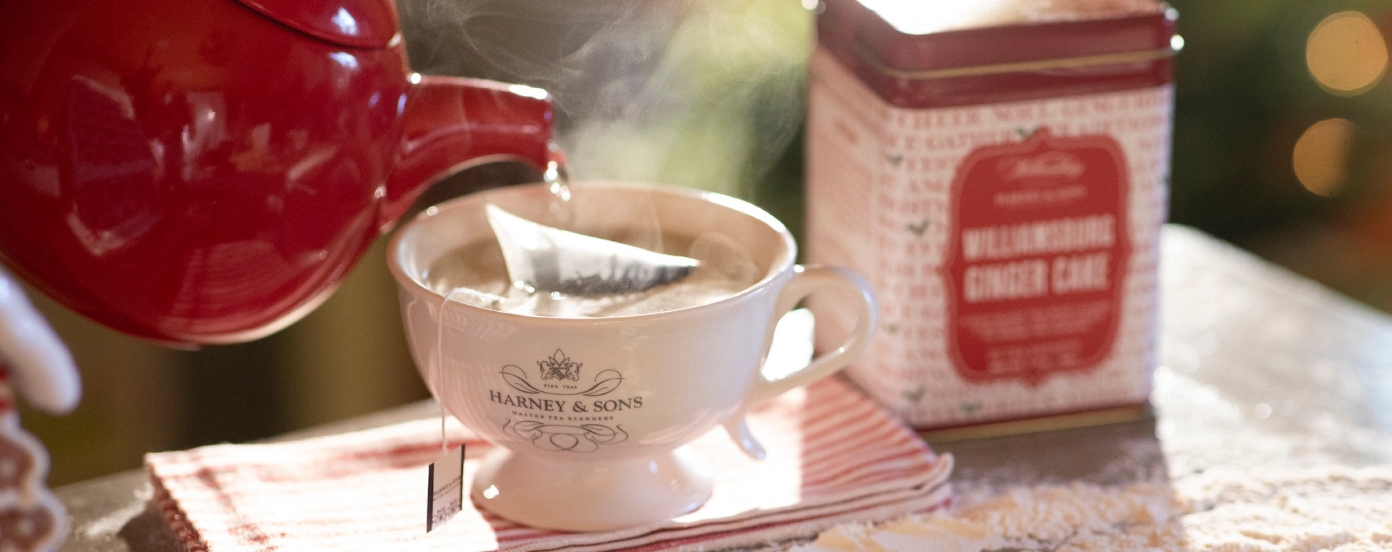 Tea cup with Harney & Sons logo, red teapot, and ginger cake tea tin on a blurred background.