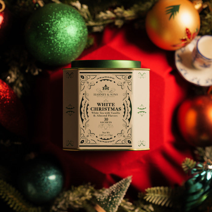 White Christmas tea tin surrounded by festive decorations on a red cloth.