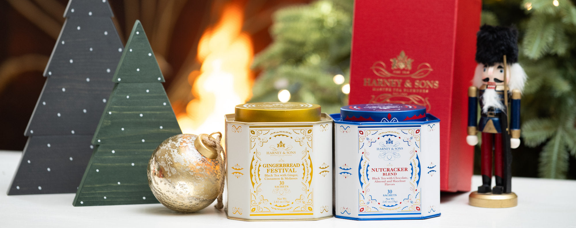 Two tea tins with decorative Christmas trees and a nutcracker in the background.