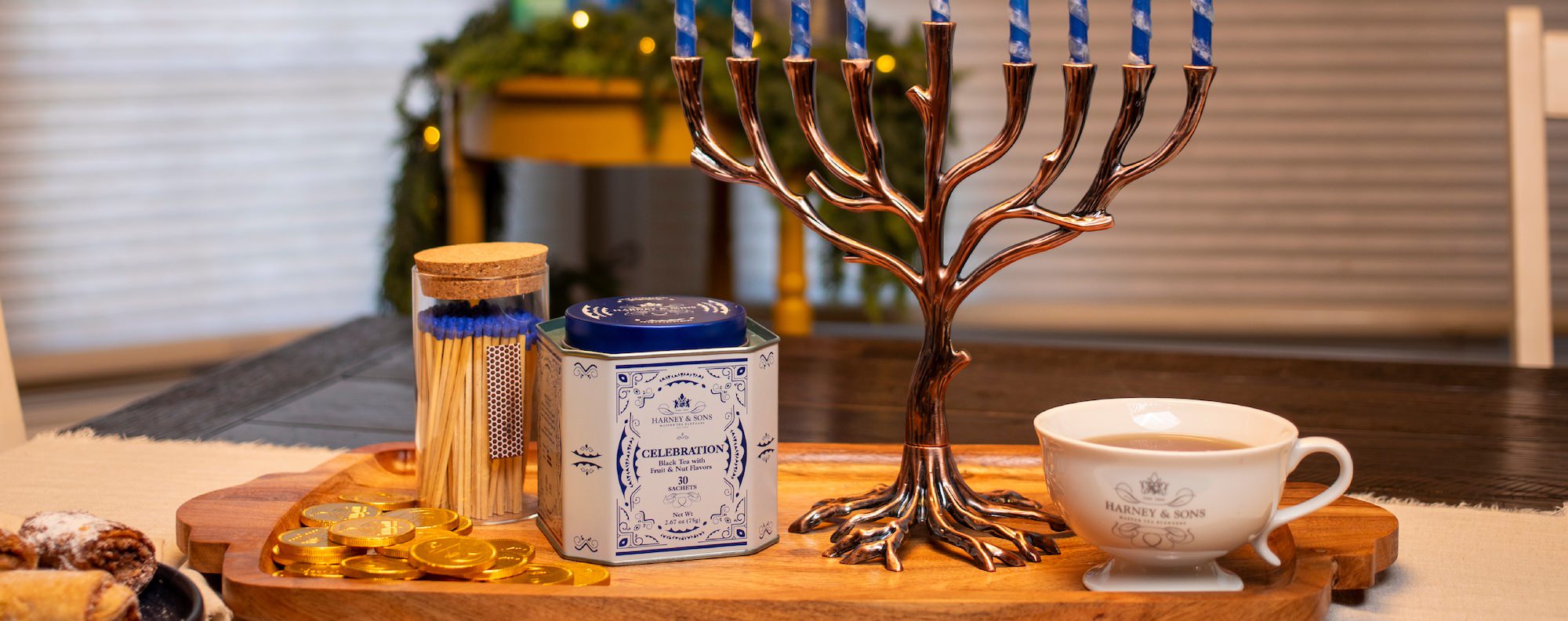 Candlelit menorah with a cup of tea on a wooden tray, surrounded by matches and a canister.