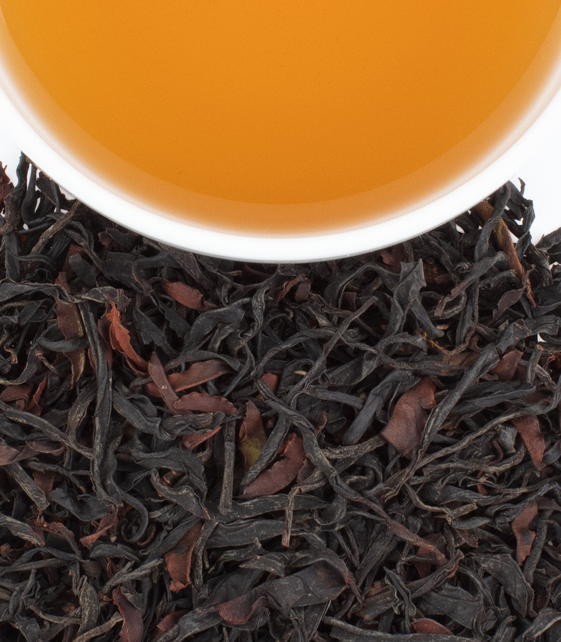 A close-up of dried black tea leaves with a cup of brewed Ancient Yunnan tea, showcasing its rich amber color.