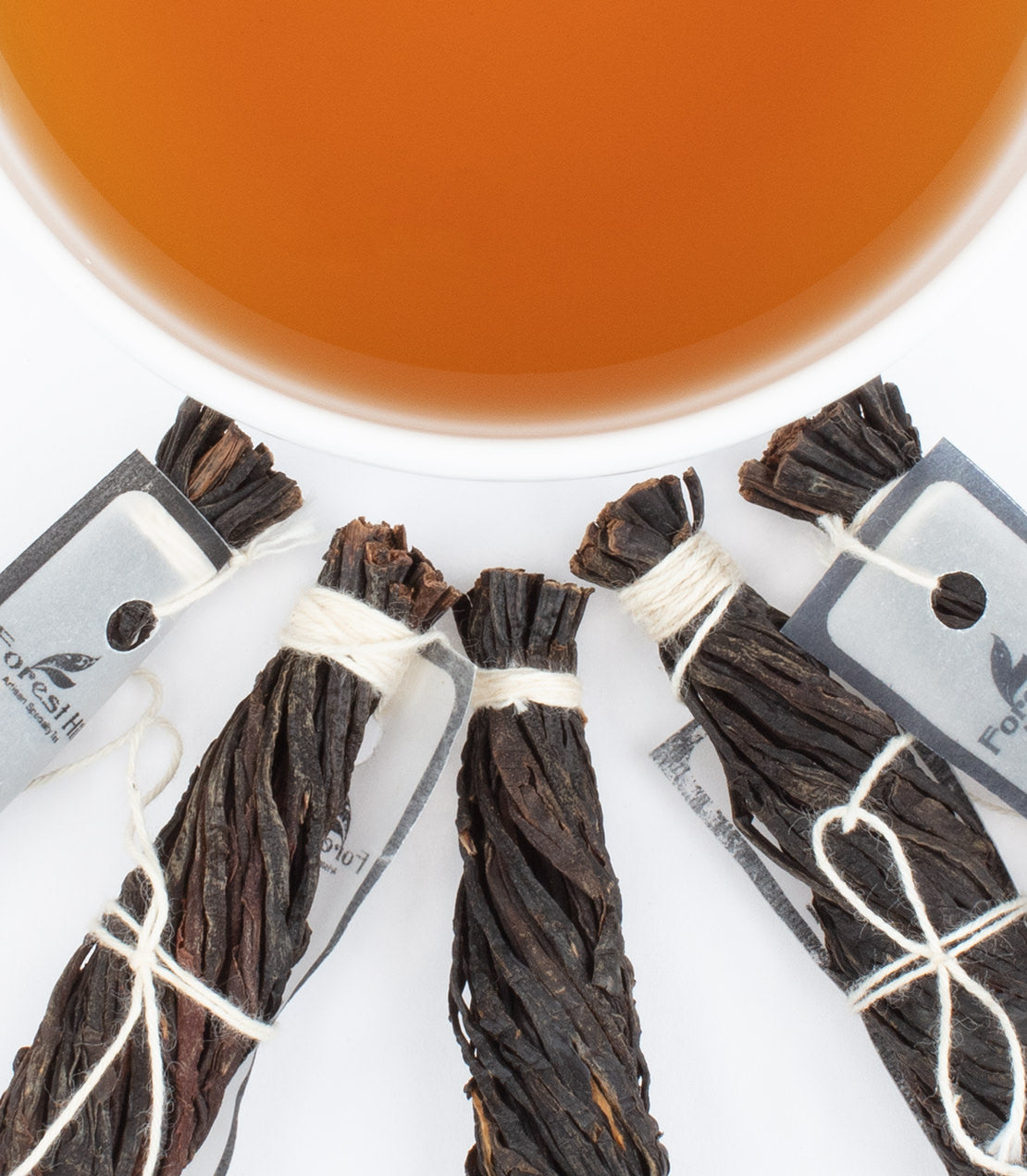 Ceylon vanilla rods arranged around a cup of tea, showcasing their rich color and packaging details.