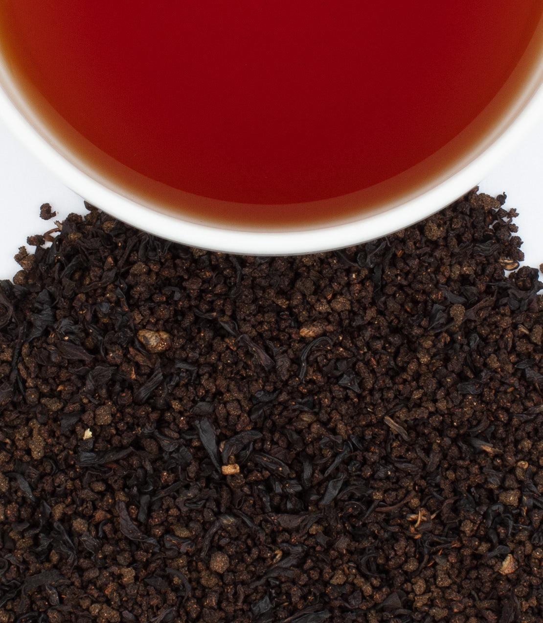 A cup of brewed chai tea sits above loose black tea leaves, showcasing rich color and texture.