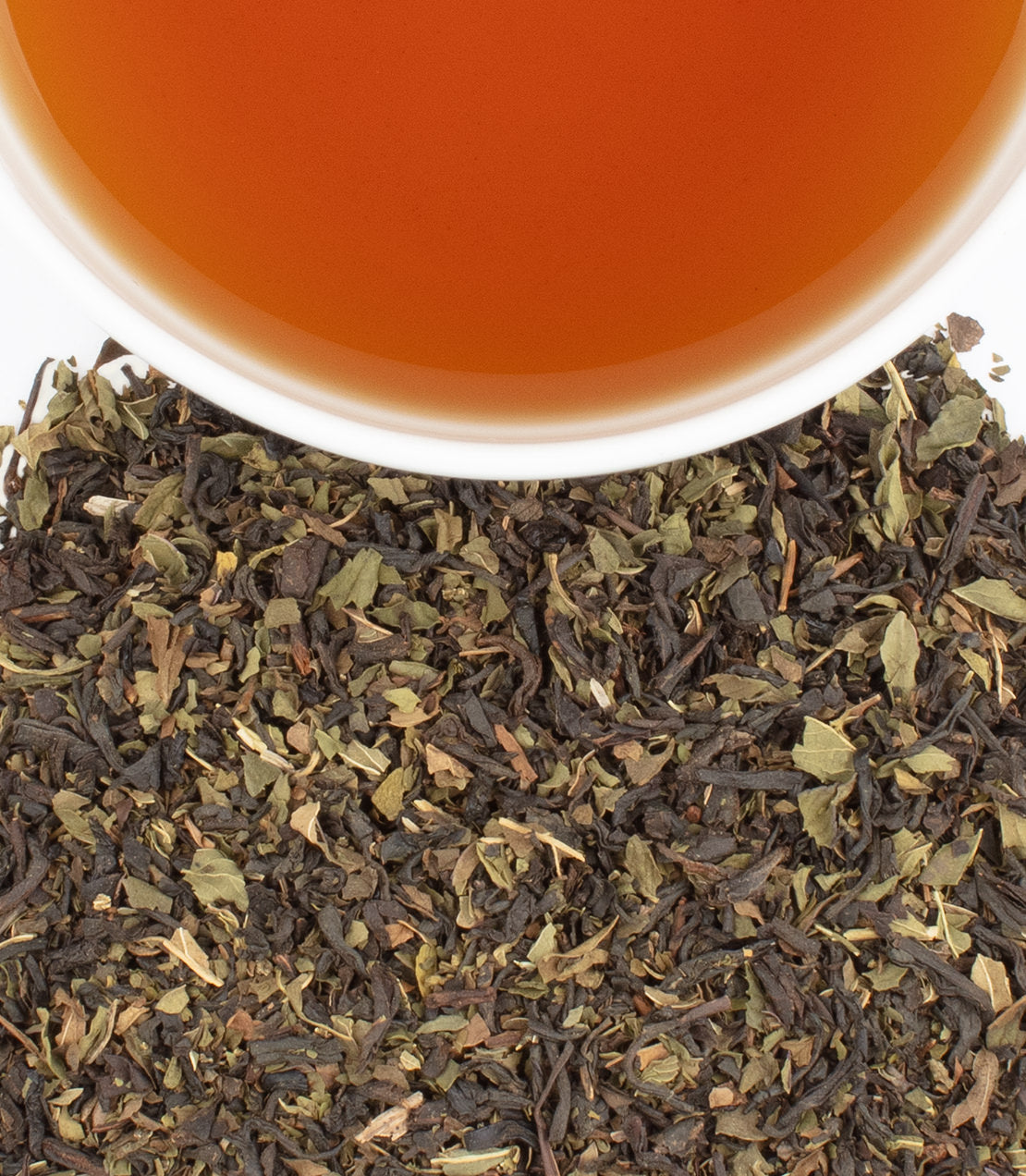 Chocolate mint tea sachets in a tin, with brewed tea in a cup above loose tea leaves.