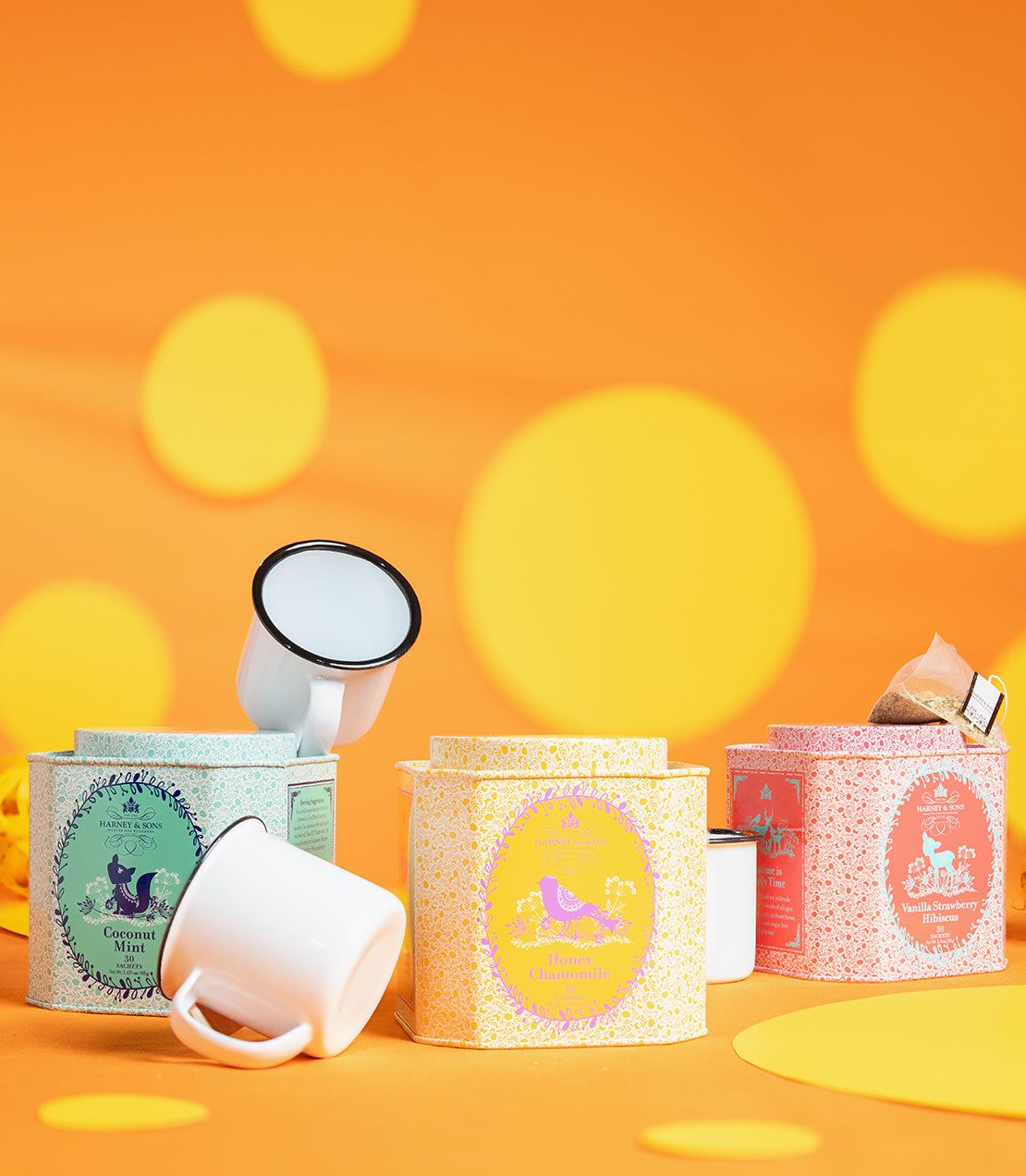 Colorful tin of Vanilla Strawberry Hibiscus tea sachets, surrounded by vibrant cups and playful polka dot background.