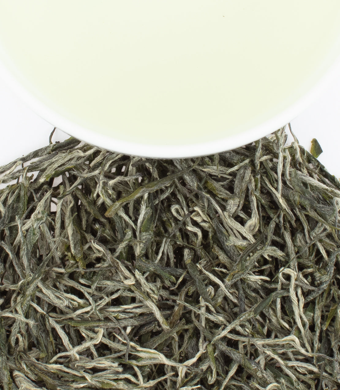 Fresh BaoMu Green tea leaves with a cup of pale green tea above, showcasing its delicate color and texture.
