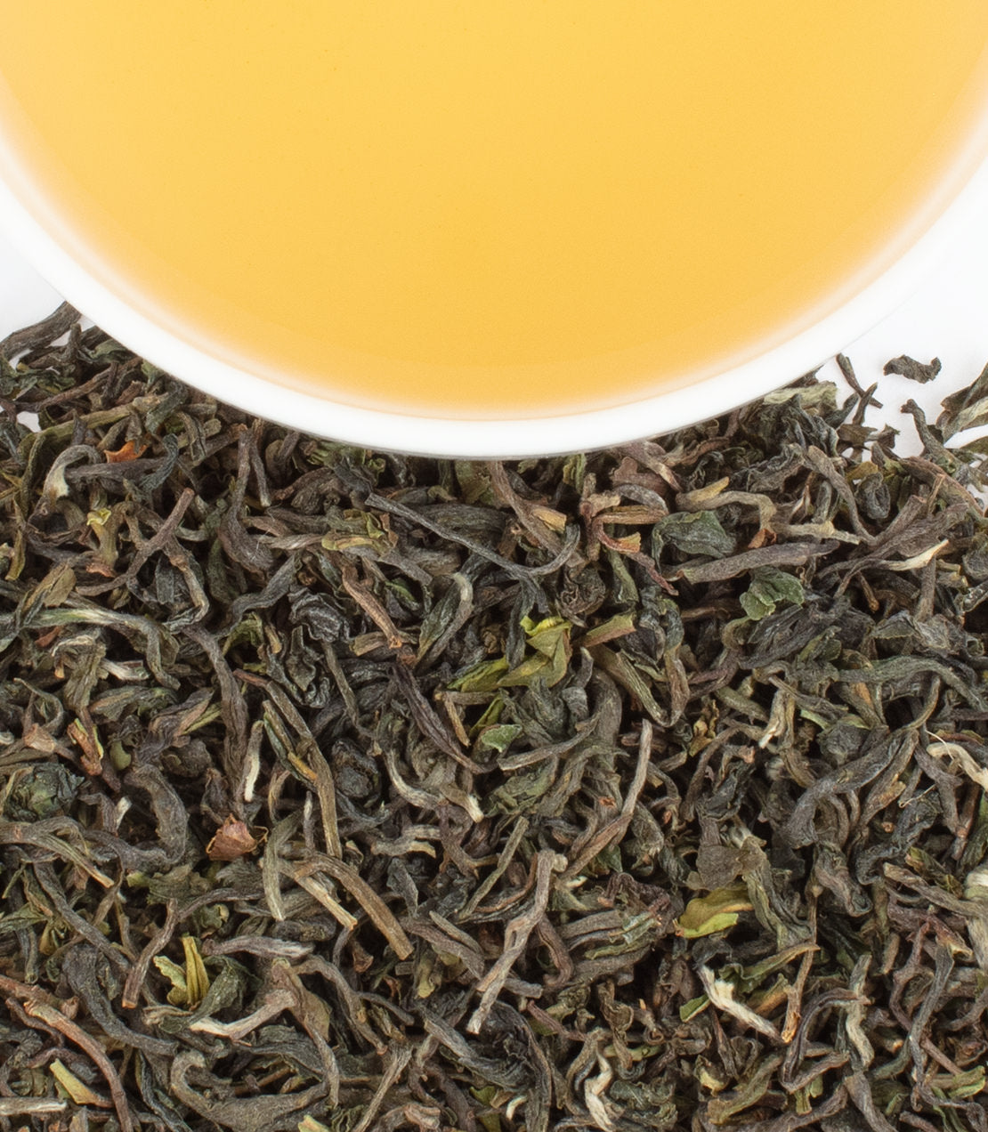 "Tukdah 1st Flush tea leaves with a cup of brewed golden tea above, showcasing its rich color and texture.