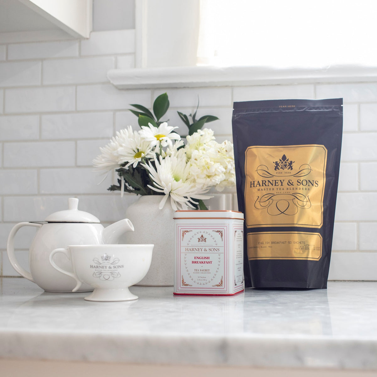English Breakfast Bag of 50 Sachets on a kitchen counter beside an English Breakfast tin, a teapot, a teacup, and white flowers