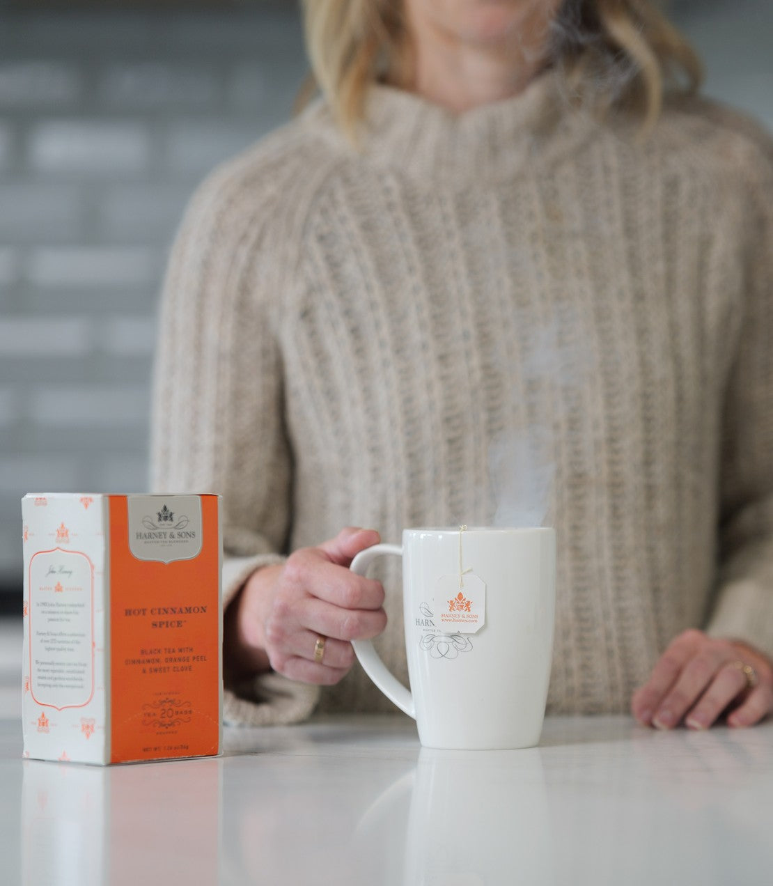 Hot Cinnamon Spice Premium Teabags, Box of 20, beside a steaming white mug with a Harney & Sons teabag tag on a kitchen counter