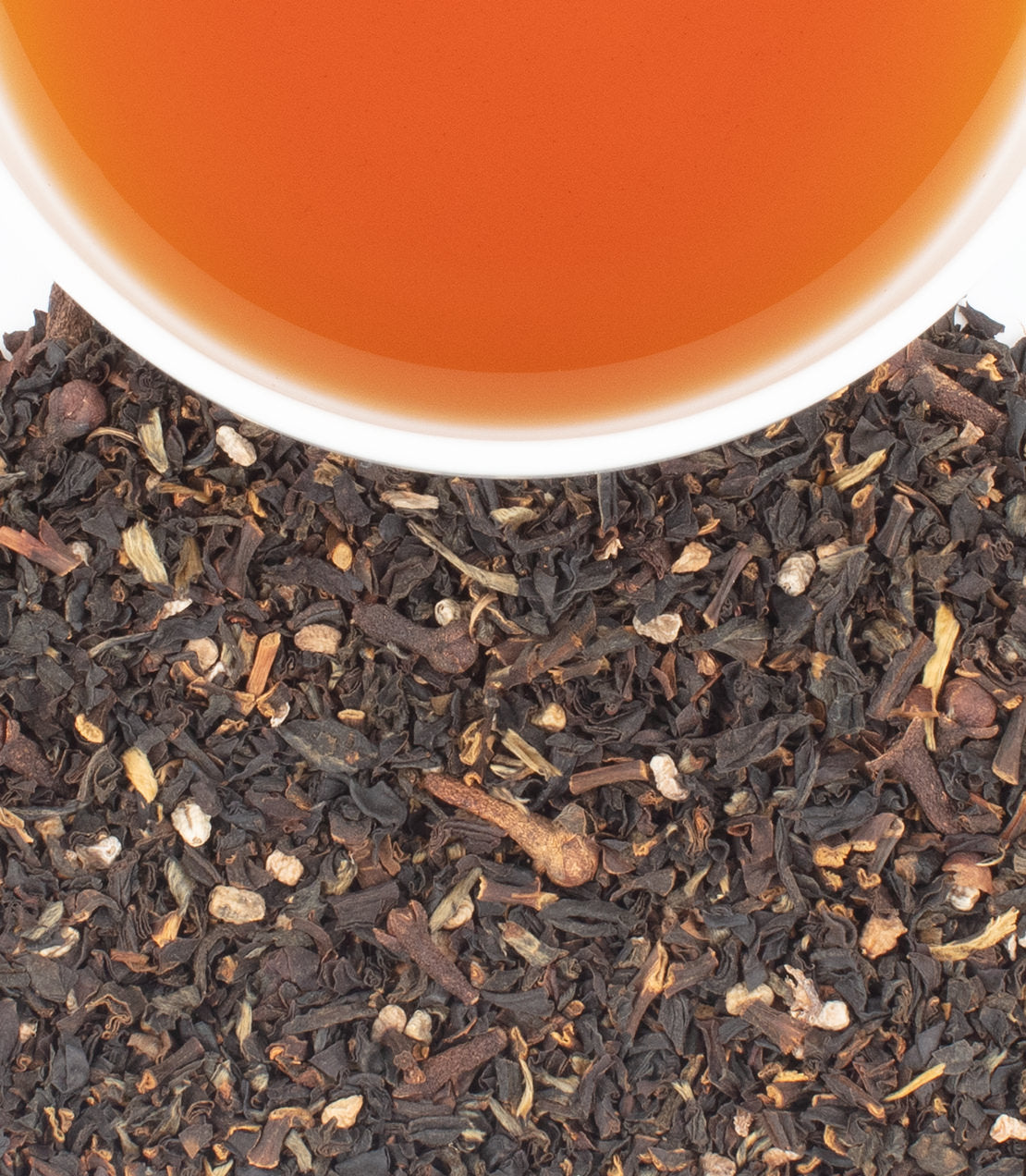 A close-up of loose Wild Spiced Ceylon tea leaves with a cup of brewed tea above, showcasing rich colors and textures.