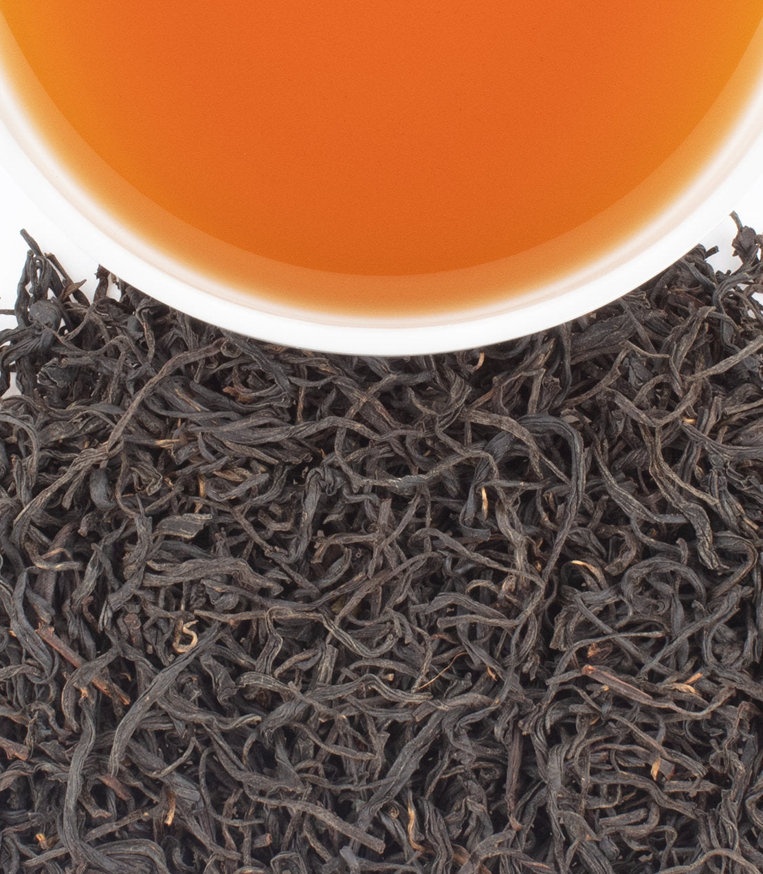 Freshly brewed Artisanal Qi Men Town tea in a white cup, surrounded by loose tea leaves.