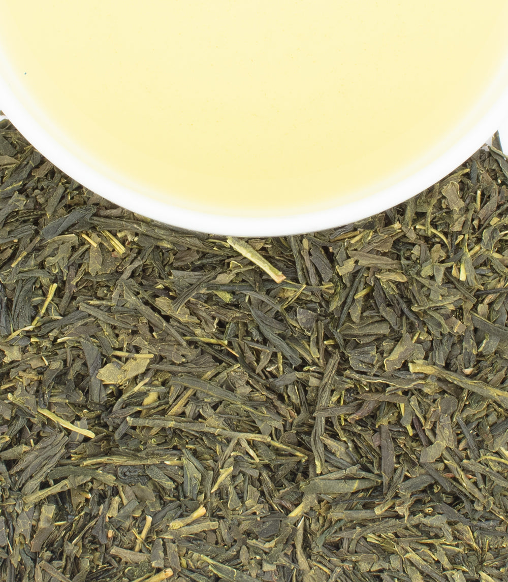 Freshly brewed Bancha green tea in a white cup, surrounded by loose Bancha tea leaves.