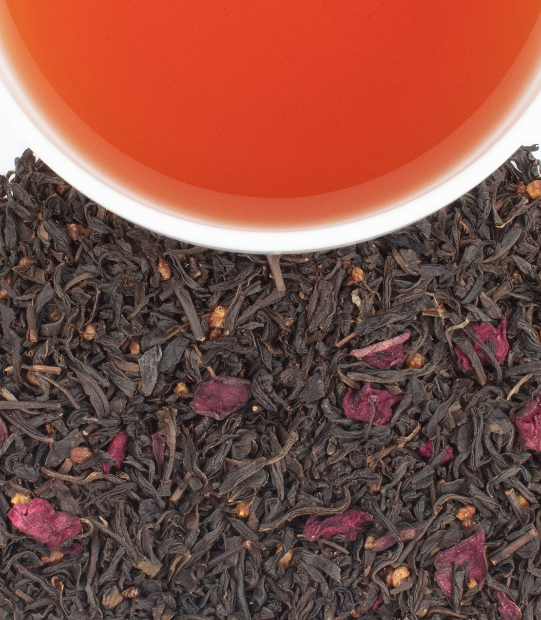 Harney & Sons Fine Teas- Brittany- A cup of vibrant orange tea sits above a pile of dark tea leaves mixed with dried purple flower petals.