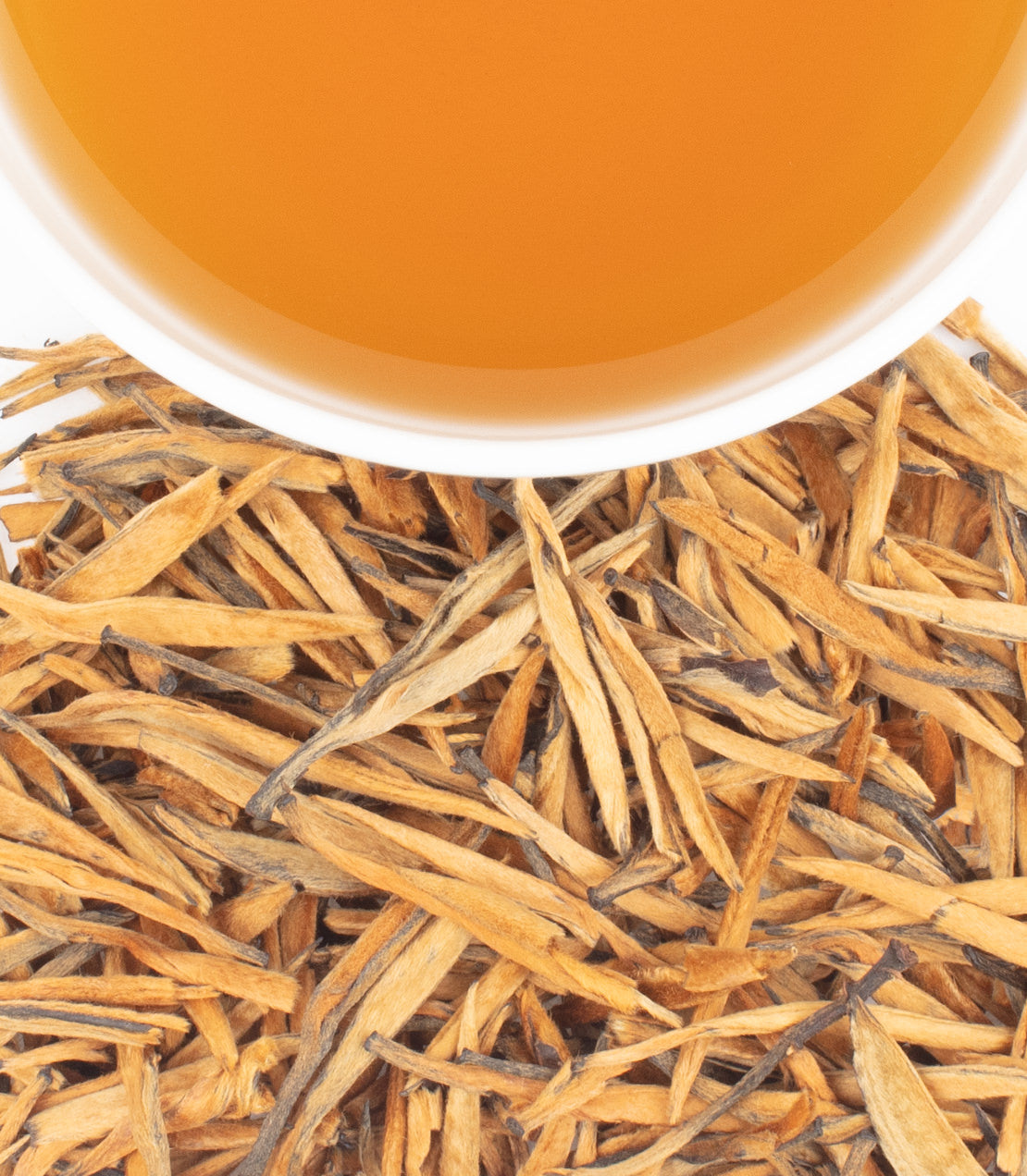 A cup of golden tea sits above a pile of dried, slender tea leaves.