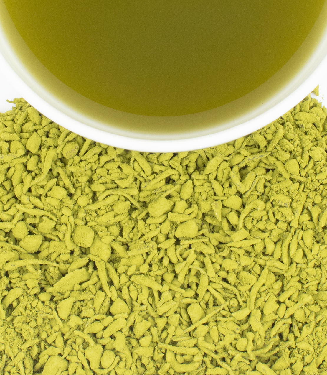 A close-up of loose green matcha powder on tea spread across the surface beneath the rim of a white cup filled with the same green tea liquid.