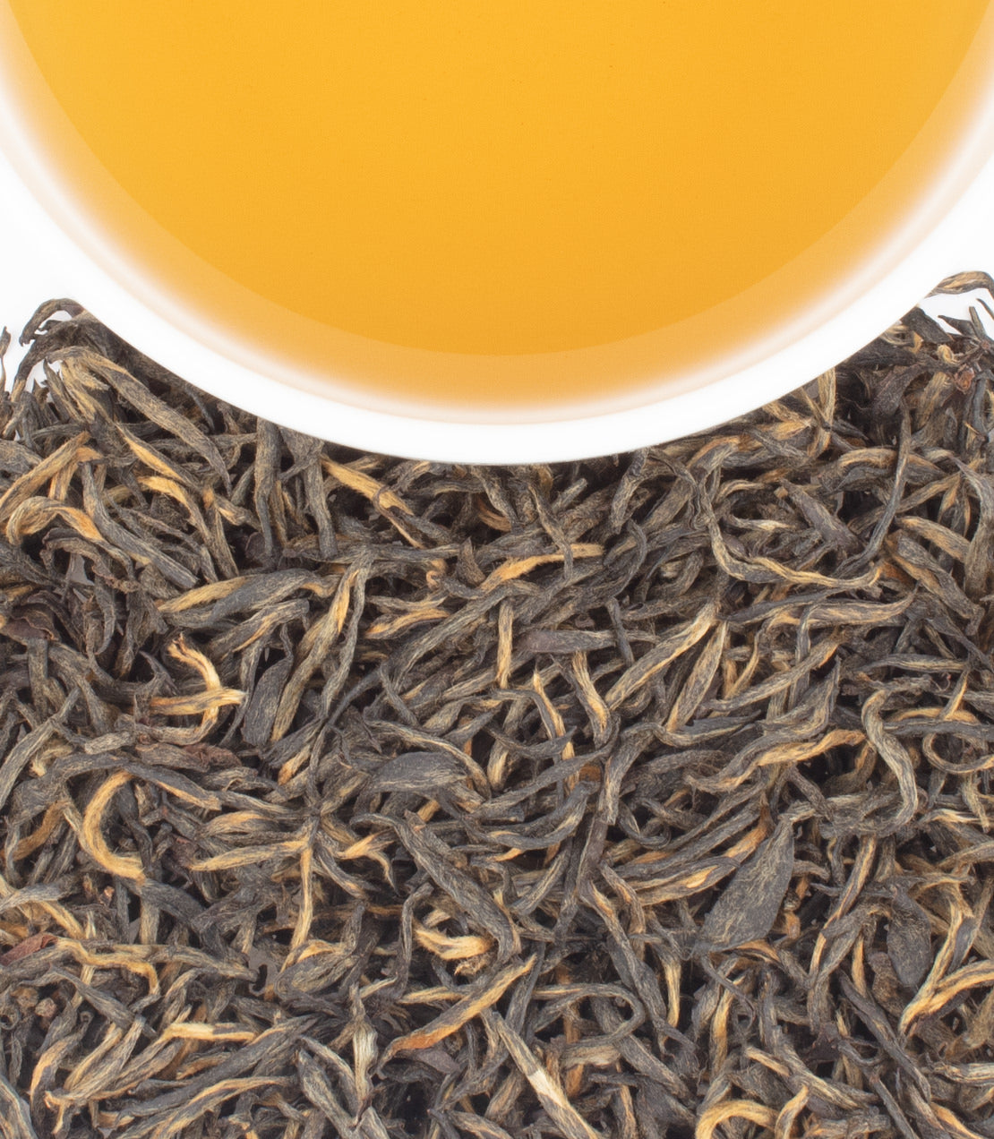 A cup of golden tea sits above a pile of dark, curly tea leaves.